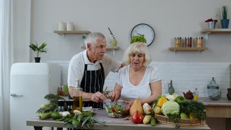 Ältere-Großeltern-In-Der-Küche.-Lustiger-Opa-Macht-Witze-über-Oma.-Legt-Ihr-Einen-Salat-über-Den-Kopf