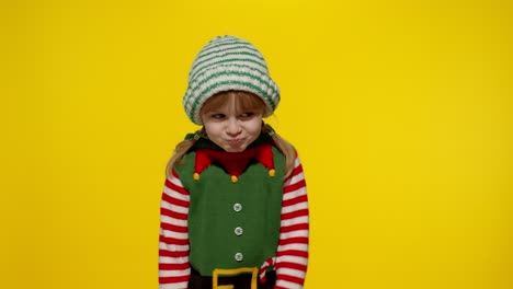 Una-Niña-Descontenta-Vestida-Con-Un-Disfraz-De-Elfo-Navideño-De-Ayudante-De-Papá-Noel-Mantiene-El-Pulgar-Hacia-Abajo-Y-Muestra-Un-Gesto-De-Disgusto