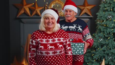 Grandfather-covering-eyes-of-old-grandmother-with-surprise-Christmas-gift-present-box-at-home-room