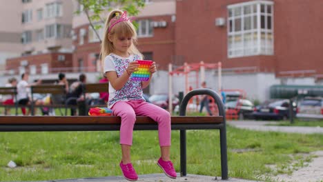 Stylish-little-child-kid-play-with-trendy-pop-it-bubble-squishy-sensory-toy-game-on-playground-bench