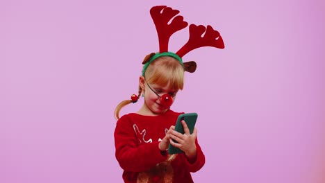 Niña-En-Navidad-Astas-De-Ciervo-Mirando-La-Pantalla-Del-Teléfono-Inteligente-Regocijándose-Sinceramente-Ganar-éxito-Suerte