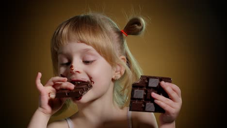 Feliz-Niña-Sonriente-Comiendo-Postre-De-Barra-De-Chocolate-Con-Leche-Aislado-Sobre-Fondo-Oscuro