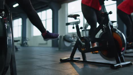 Close-up-legs-of-group-unrecognizable-friends-at-gym-exercising-on-stationary-bike-at-class-in-gym