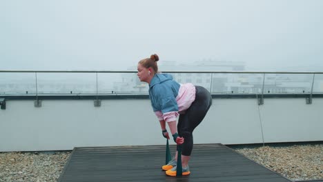 Una-Chica-Deportiva-Con-Ropa-Deportiva-Hace-Ejercicios-De-Estiramiento-De-Yoga-Usando-Una-Banda-Elástica-En-El-Techo-De-La-Casa-Al-Aire-Libre