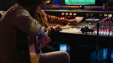 Creative-musician-singing-guitar-in-professional-studio-control-room