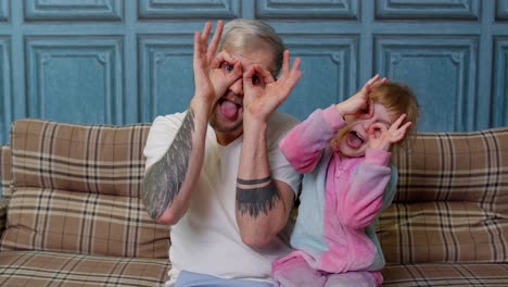 Father-and-child-daughter-kid-in-pajamas-fooling-sit-on-couch-in-living-room-smile-look-at-camera