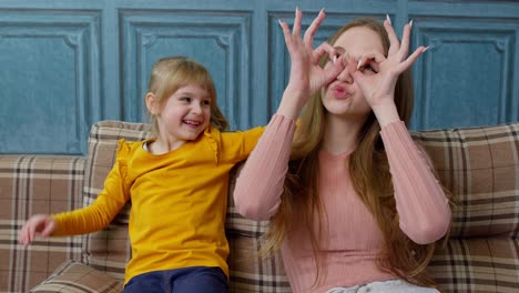 Mother-and-little-child-kid-daughter-having-fun-sitting-on-sofa-fooling-around,-making-faces-at-home