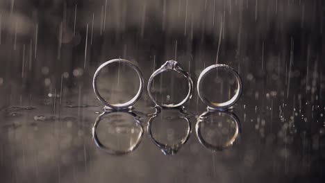 Wedding-and-engagement-rings-lying-on-dark-water-surface-shining-with-light