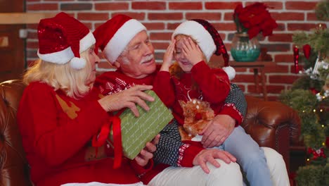 Abuelos-Regalando-Una-Caja-De-Regalo-De-Navidad-A-Una-Nieta-Feliz-Y-Sorprendida-En-Casa,-Celebrando