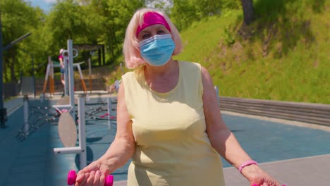 Senior-woman-grandmother-doing-training-weightlifting-exercising-with-dumbbells-on-park-playground