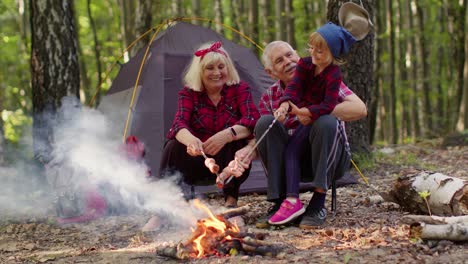 Senior-Großmutter-Großvater-Mit-Enkelin-Kochen-Bratwürste-über-Lagerfeuer-Im-Holz