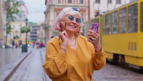 Senior-man-tourist-with-retro-photo-camera,-smiling,-listening-music-earphones,-dancing-on-street