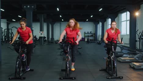 Group-of-girls-performs-aerobic-training-workout-cardio-routine-on-bike-simulators,-cycle-training