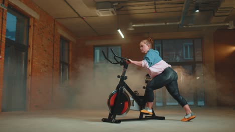 Mujer-Atlética-Montando-Una-Rutina-De-Entrenamiento-En-Bicicleta-Estacionaria-Giratoria-En-Un-Gimnasio-De-Niebla,-Pérdida-De-Peso-En-Interiores