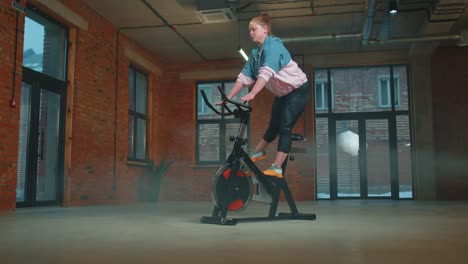 Healthy-Caucasian-woman-exercising-workout-on-stationary-cycling-machine-bike-in-gym,-Slow-Motion