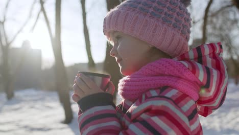 Niña-Sonriente-Bebiendo-Té-Caliente-De-Una-Taza,-Tratando-De-Mantenerse-Caliente-En-El-Bosque-Del-Parque-De-Invierno