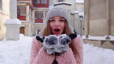 Young-woman-traveler-tourist-showing-snow-in-hands-palms-to-camera-and-blowing-it-on-city-street