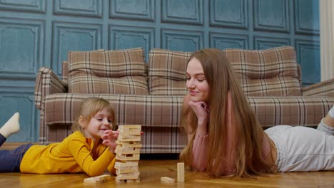 Feliz-Joven-Madre-Enseñando-A-Su-Hija-Pequeña-A-Jugar-Juegos-De-Mesa-Con-Bloques-De-Madera-En-Casa