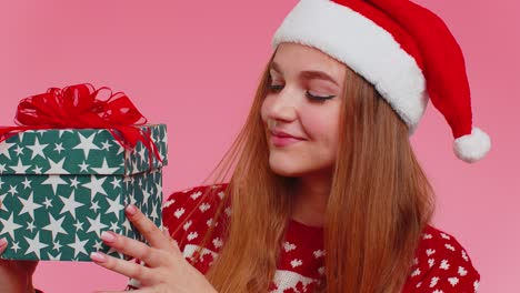 Una-Chica-Alegre-Y-Encantadora-Con-Un-Suéter-Con-Sombrero-De-Papá-Noel-Presentando-Una-Caja-De-Navidad,-Emocionada-Por-El-Regalo-Navideño