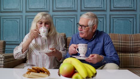 Mature-family-couple-grandfather,-grandmother-relaxing-on-cozy-sofa-enjoying-conversation-at-home