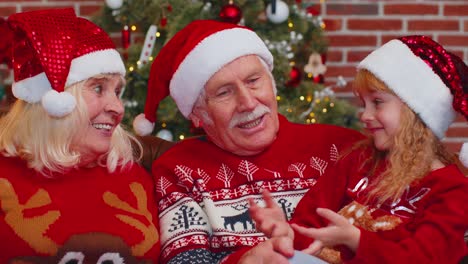 Happy-senior-grandparents-with-granddaughter-enjoying-pleasant-conversation-in-Christmas-home-room