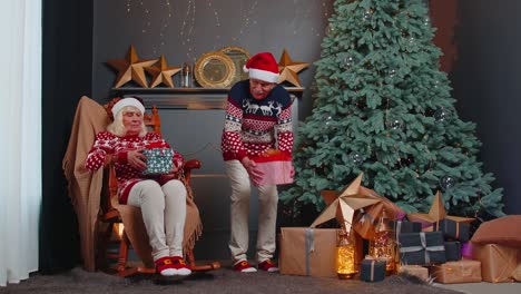 Senior-family-couple-grandmother-grandmother-presenting-Christmas-gift-boxes-to-each-other-at-home