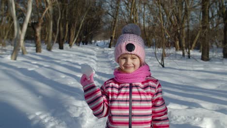 Niña-Lanzando-Bolas-De-Nieve-Hacia-La-Cámara,-Niño-Sonriente-Caminando,-Jugando-Con-Nieve-En-El-Parque-De-Invierno