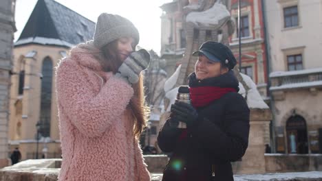 Dos-Mujeres-Turistas-Sonrientes-Viajando-Juntas,-Bebiendo-Té-Caliente,-Café-De-Termo-En-La-Calle-De-La-Ciudad