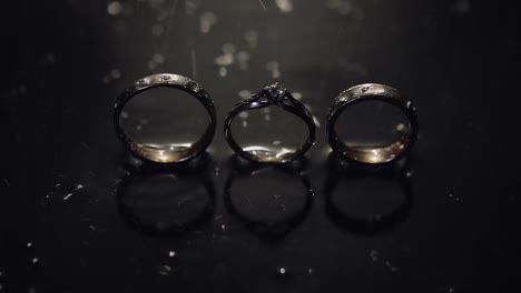 Anillos-De-Boda-Y-Compromiso-Sobre-Una-Superficie-De-Agua-Oscura-Brillando-Con-Luz