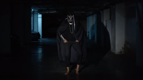 Creepy-scary-man-in-skeleton-Halloween-makeup-dancing-against-dark-parking-hallway-in-slow-motion