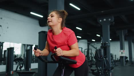 Mujer-Joven-Atlética-Montando-En-Rutina-De-Entrenamiento-De-Bicicleta-Estacionaria-Giratoria-En-El-Gimnasio,-Pérdida-De-Peso-En-Interiores