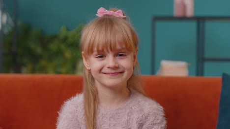 Portrait-of-little-adorable-child-girl-sitting-alone-on-sofa-at-home-looking-at-camera-and-smiling