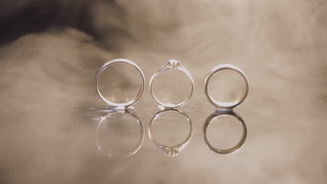 Anillos-De-Boda-Y-Compromiso-Sobre-Una-Superficie-De-Agua-Oscura-Brillando-Con-Luz