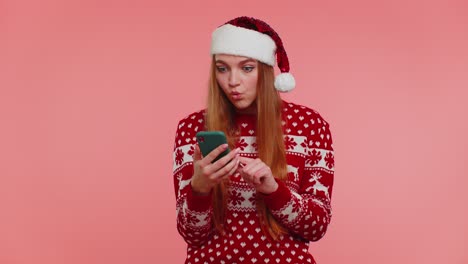 Una-Chica-Adulta-Con-Un-Suéter-Navideño-Mirando-La-Pantalla-Del-Teléfono-Inteligente-Regocijándose-Sinceramente-Por-Ganar-éxito-Y-Suerte