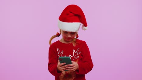 Chica-Feliz-En-Un-Suéter-De-Ciervo-Navideño-Mirando-La-Pantalla-Del-Teléfono-Inteligente-Regocijándose-Sinceramente-Por-Ganar-éxito-Y-Suerte