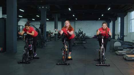 Grupo-Caucásico-Saludable-De-Mujeres-Haciendo-Ejercicio-En-Bicicleta-Estática-En-El-Gimnasio