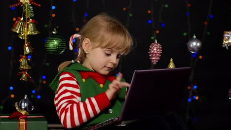 Kid-girl-in-Christmas-elf-costume-doing-shopping-online-using-laptop,-browsing-on-social-media