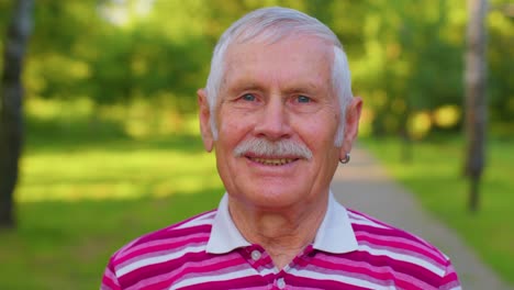 Lovely-cheerful-senior-old-gray-haired-grandfather-in-casual-red-t-shirt-on-summer-park-background