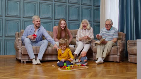 Ocio-Familiar-Multigeneracional-En-Casa,-Motivando-Gritos-A-Una-Niña-Jugando-Juguete-Ferroviario