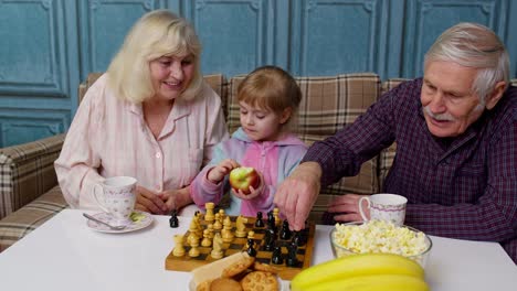 Abuela-Madura-Abuelo-Con-Niña-Nieta-Jugando-Ajedrez-Con-Sobre-La-Mesa-En-La-Habitación