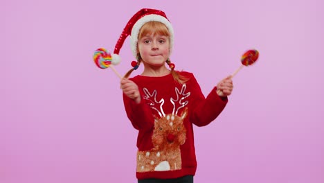 Joyful-girl-in-Christmas-sweater,-hat-holding-candy-striped-lollipops,-dancing,-making-silly-faces