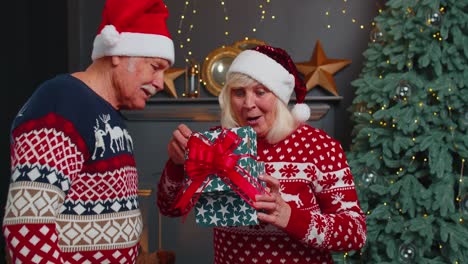 Abuelo-Regalando-Caja-De-Regalo-De-Navidad-A-Abuela-Sorprendida,-Feliz-Pareja-De-Ancianos-Con-Sombreros