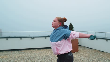 Sporty-girl-in-sportswear-does-yoga-stretching-exercising-using-rubber-band-on-roof-of-house-outdoor