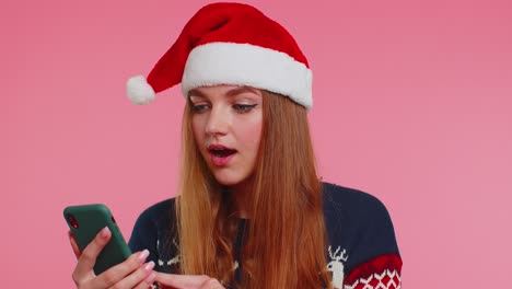 Frau-Im-Stilvollen-Weihnachtspullover-Schaut-Auf-Das-Smartphone-Display-Und-Freut-Sich-Aufrichtig-über-Den-Sieg,-Den-Erfolg-Und-Das-Glück