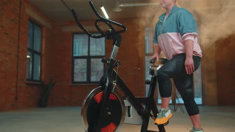 Chica-Atlética-Realizando-Ejercicios-De-Entrenamiento-Aeróbico-En-Bicicleta-Estática-En-Un-Gimnasio-Con-Niebla