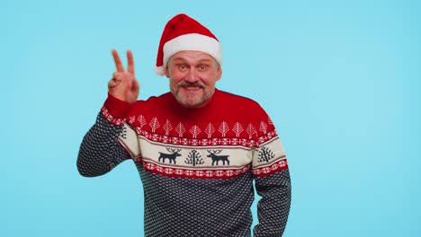 Un-Hombre-Positivo-Con-Un-Suéter-Navideño-Con-Ciervos-Ondea-La-Palma-De-La-Mano-En-Un-Gesto-De-Saludo-Y-Le-Da-La-Bienvenida-A-Alguien