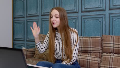 Girl-waving-her-hand-hi-hello,-talking-looking-into-laptop-computer,-video-call-with-teacher