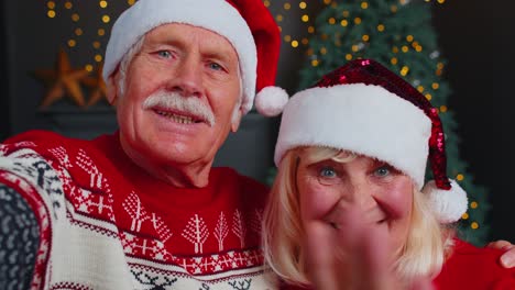 Mature-couple-family-in-Santa-Claus-hats-celebrating-Christmas-looking-at-camera-and-hugging-at-home