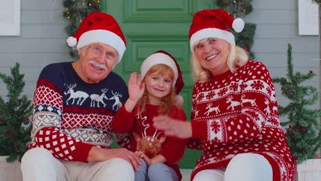 Pareja-De-Ancianos-Abuelos-Con-Nieta-Niña-Saluda-Con-La-Mano,-Hola-Cerca-De-La-Casa-De-Navidad