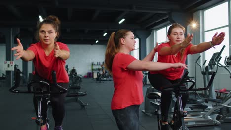 Group-of-girls-performs-aerobic-training-workout-cardio-routine-on-bike-simulators,-cycle-training